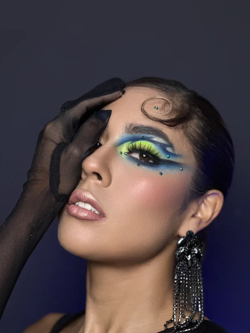 Maquillaje artístico verde y azul neón con pedrería sobre el párpado